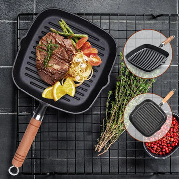 Square grill pan with wooden handle featuring seared steak, vegetables, and lemon garnish on dark tile surface, with product 