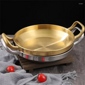 Golden stainless steel wok pan with brass handles on wooden trivet, styled with red tomatoes and gray linen cloth.