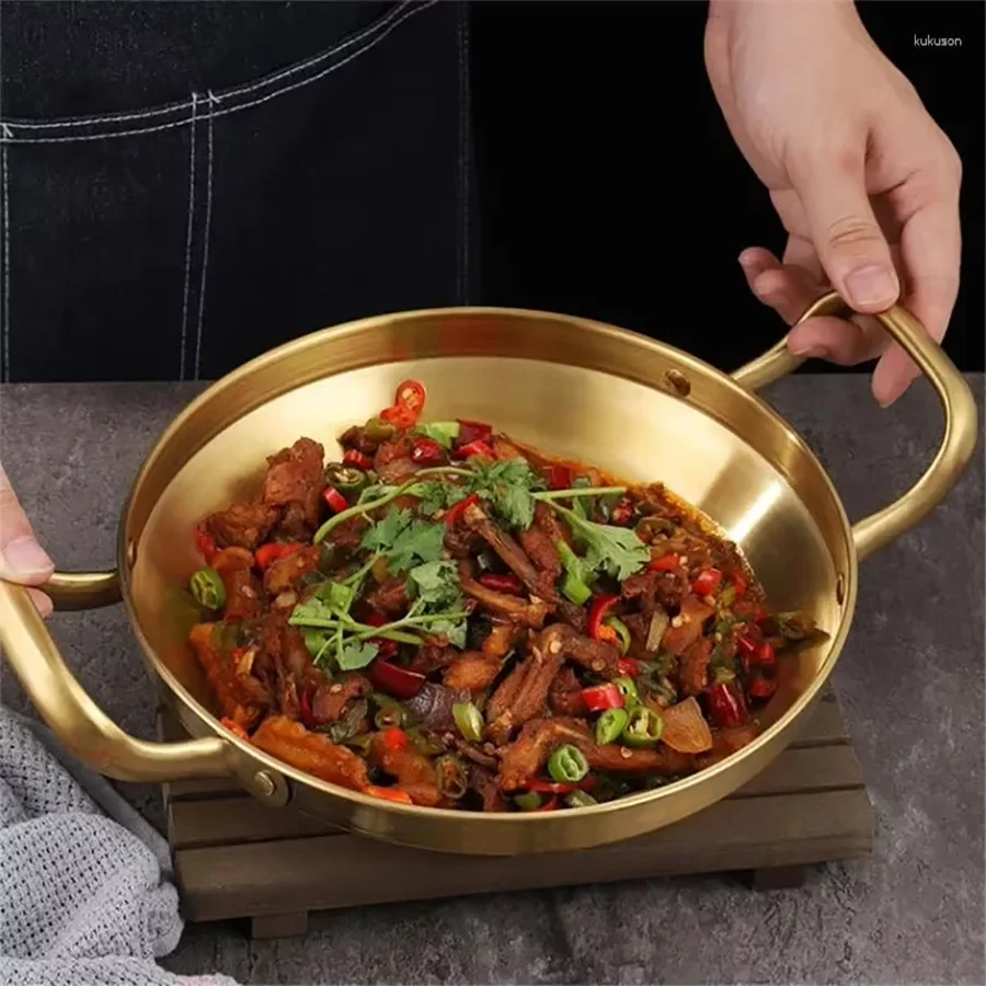 Golden stainless steel wok pan with handles displaying cooked stir-fry with vegetables and meat garnished with cilantro and c