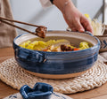 Blue and tan earthenware clay casserole pot with noodle soup, chopsticks lifting meat, on woven placemat