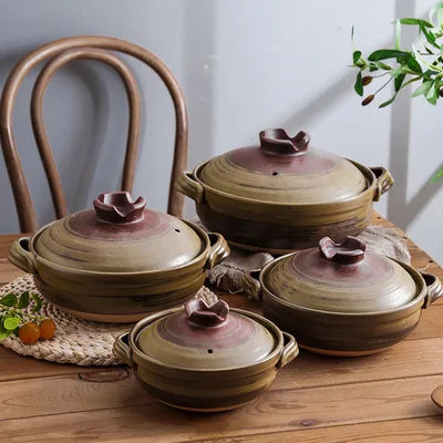 Four earthenware clay casserole pots in graduated sizes with burgundy flower-shaped lids, displayed on wooden table with wove