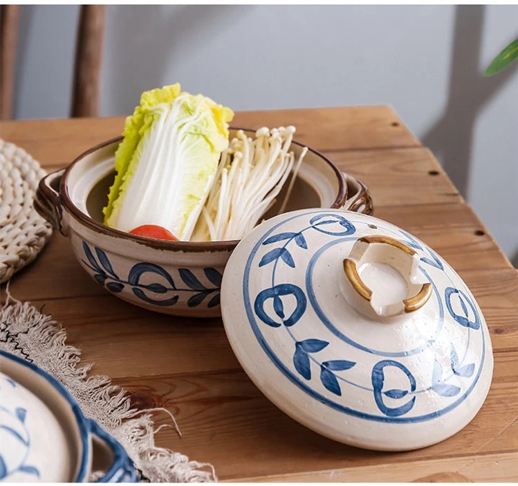 Blue and white ceramic clay casserole pot with lid containing napa cabbage, displayed on wooden table with neutral linens.