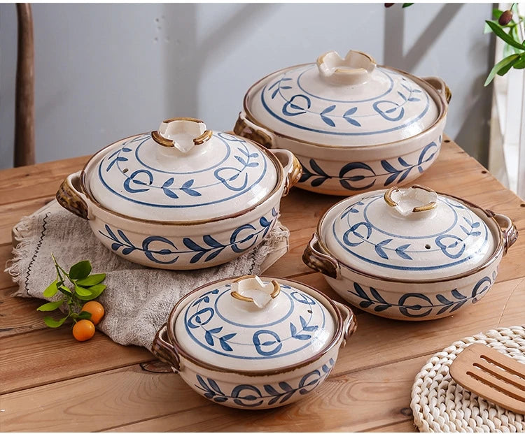 Four blue and white earthenware casserole pots with lids arranged on wooden surface, featuring leaf motifs and natural handle