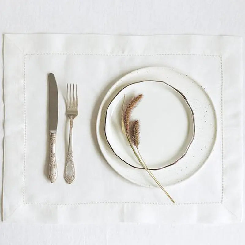 Elegant table setting with stacked cream plates, ornate silverware, and dried pampas grass on natural linen placemat