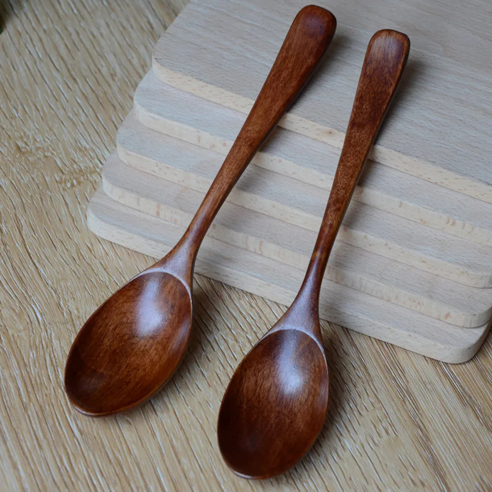 Two hand-crafted wooden cooking spoons with polished bowls and long handles, displayed on light wood surface.
