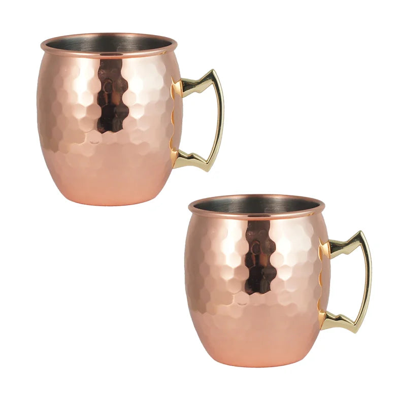 Pair of hammered copper insulated travel mugs with brass handles and stainless steel interiors, displayed against white backg