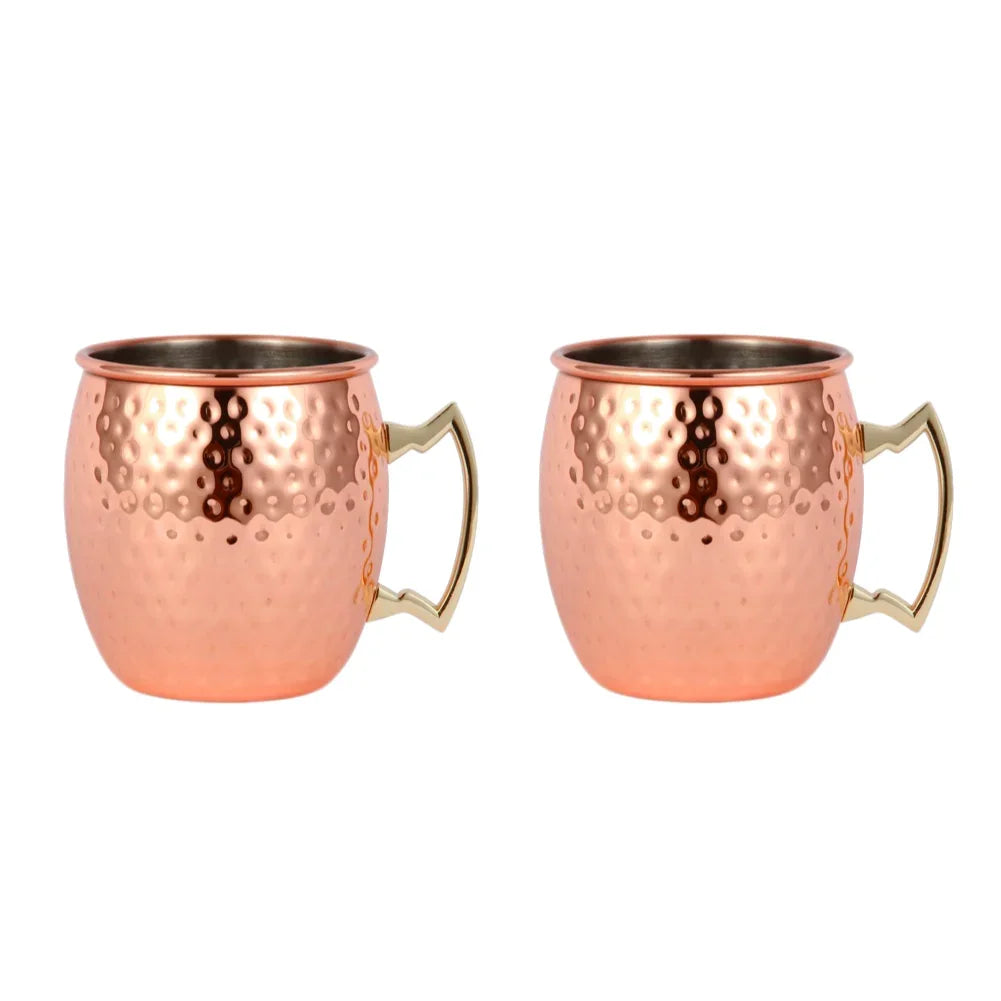 Pair of hammered copper Moscow mule mugs with brass handles and dark interior lining, isolated on white background.
