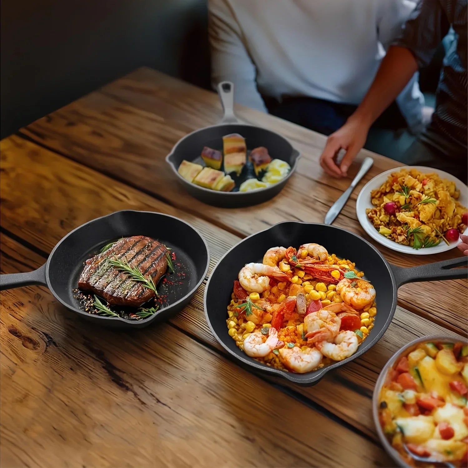 Three black cast iron skillets displaying grilled steak, shrimp with corn, and tofu on wooden table with person serving.
