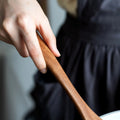 Child's hand holding wooden spatula from eco-friendly kitchen utensil set against blurred black background