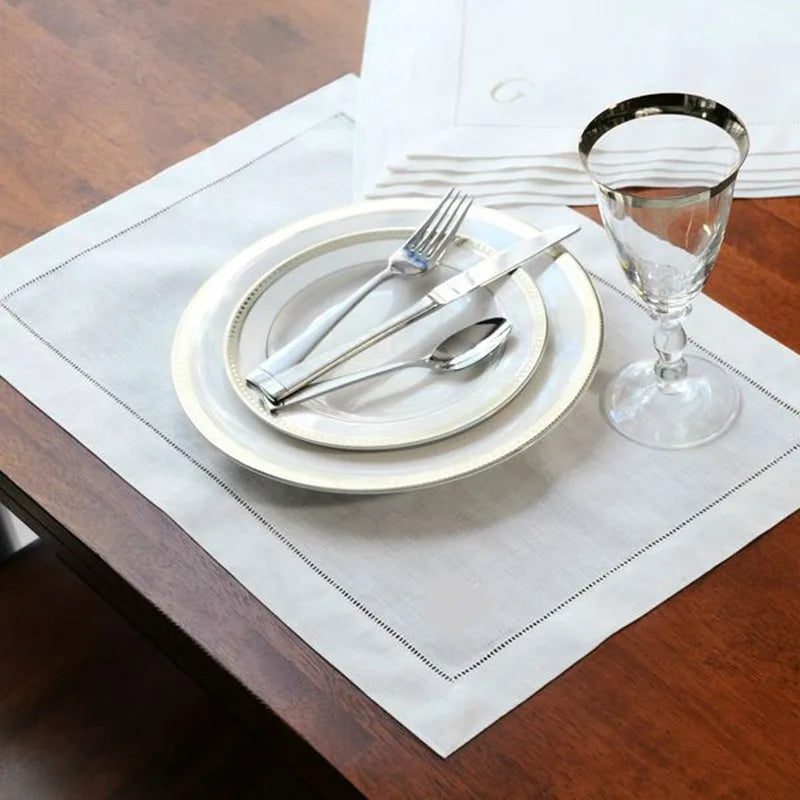 Elegant place setting with stacked white plates, silver flatware, and water glass on natural linen placemat with decorative s