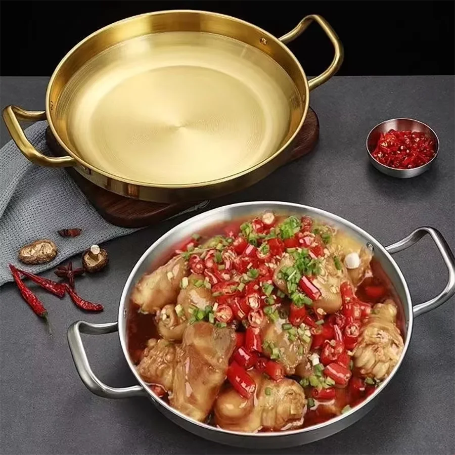 Golden stainless steel wok pan with dual handles, displayed with prepared chicken dish garnished with red chilies and green o