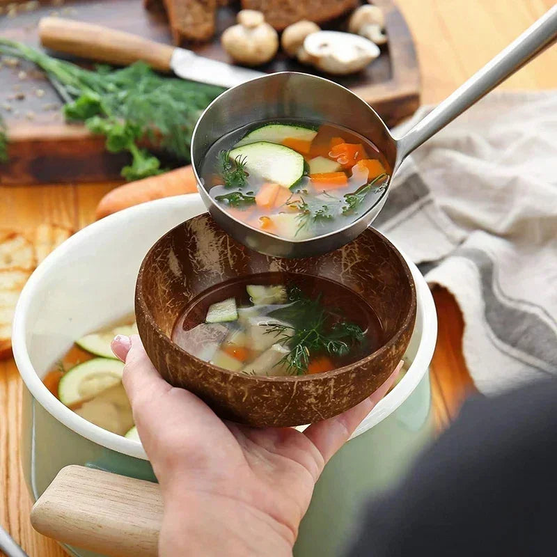 Coconut wood serving bowl filled with vegetable soup, ladle pouring broth, artisan handcrafted eco-friendly tableware set