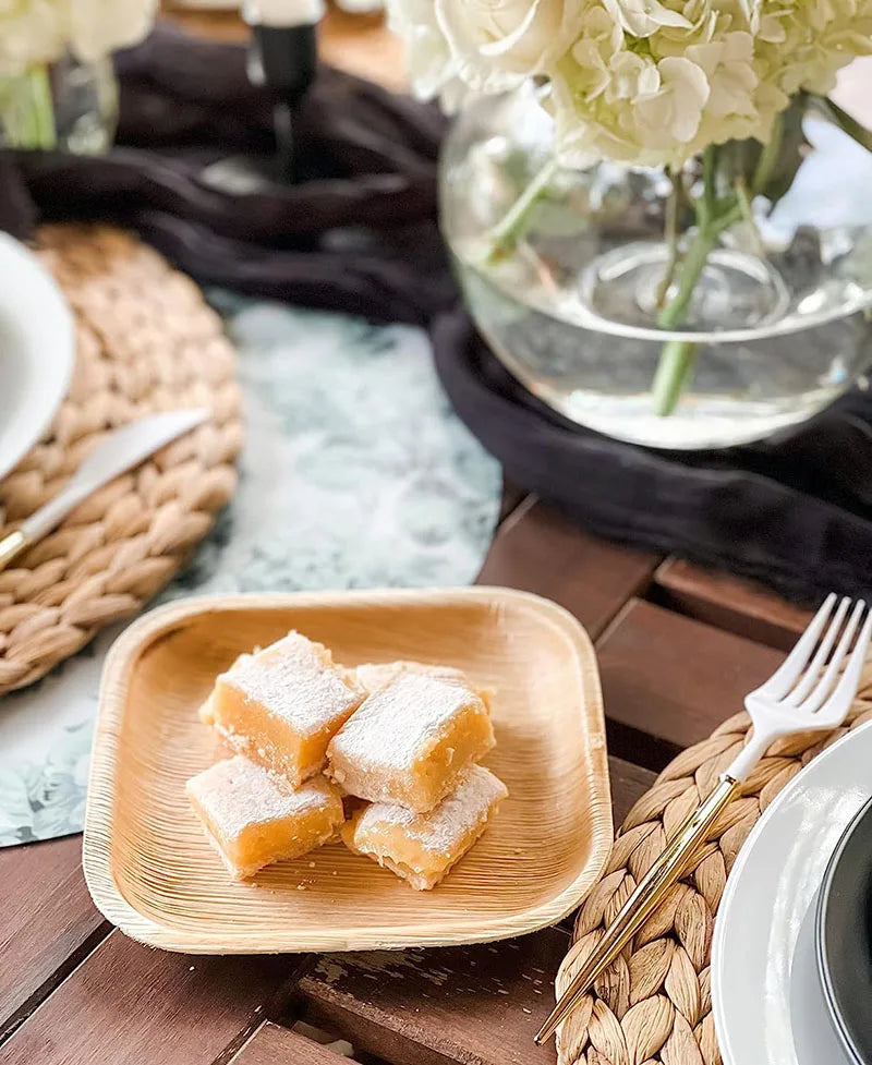 Eco-friendly palm leaf plate holding powdered lemon bars, styled on table with natural décor and white flowers.
