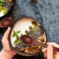 Handcrafted wooden serving bowl filled with yogurt, granola, kiwi slices, chia seeds, and almonds, with wooden spoon.