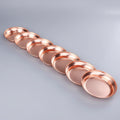 Seven handcrafted pure copper dining plates in graduated sizes arranged diagonally, showcasing rich red copper finish and pol