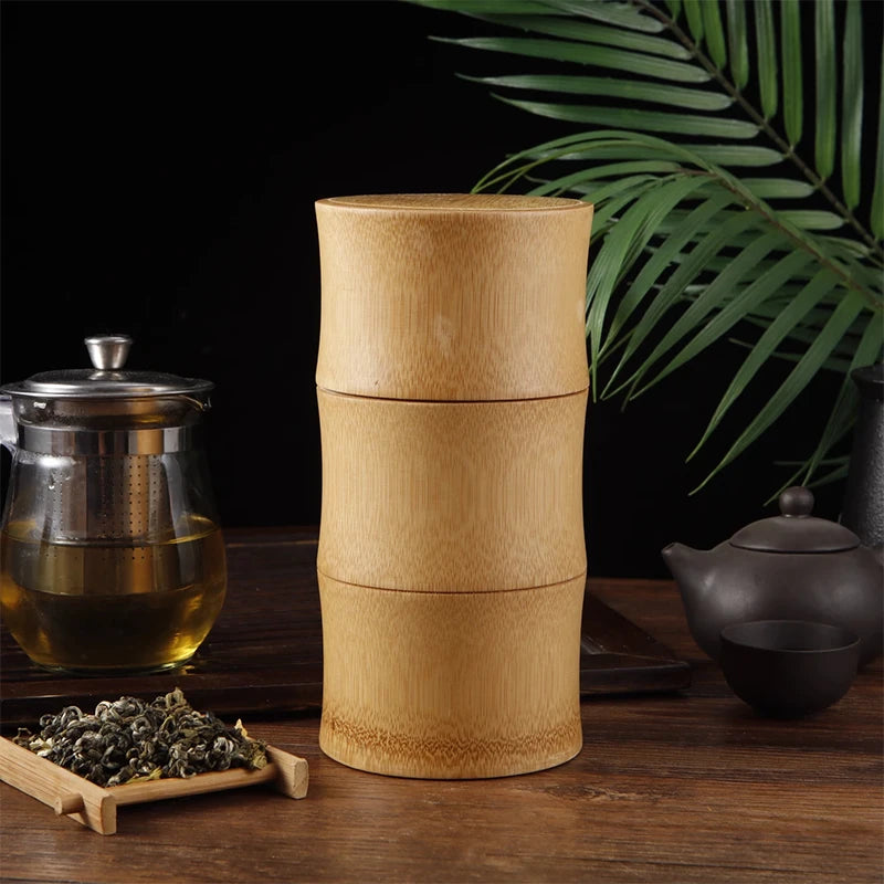 Bamboo food storage box with three stacked sections, displayed with tea leaves, glass teapot, black teapot, and green plant o