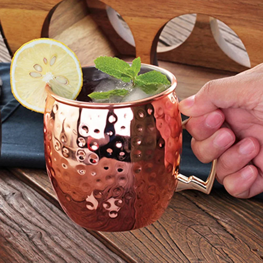 Copper Moscow mule mugs with hammered finish, filled with cranberry cocktails, ice, lime wedges, cinnamon sticks, and fresh c