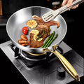 Stainless steel wok pan with golden handles cooking steak, vegetables, and garnishes on stovetop, showcasing non-stick surfac