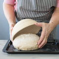 Natural rattan bread proofing basket with cloth liner being used to shape artisan dough by baker in apron.