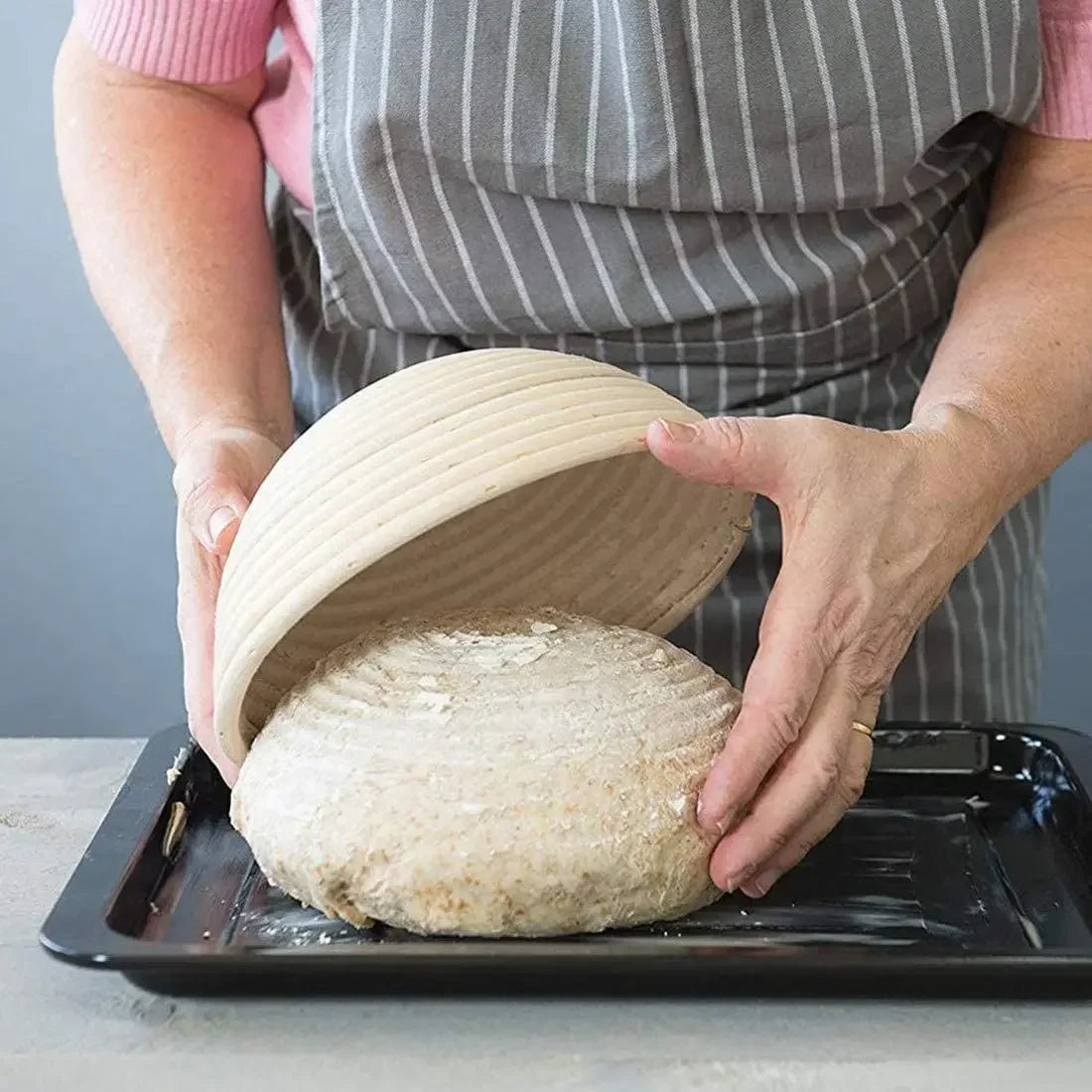 Natural rattan bread proofing basket with cloth liner being used to shape artisan dough by baker in apron.
