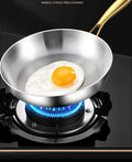 Stainless steel wok pan with golden handle cooking fried egg over blue gas flame, demonstrating non-stick surface and heat di