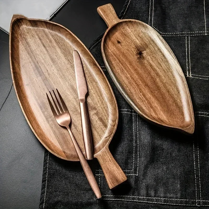 Handcrafted wooden palm leaf-shaped dessert tray with handle, displayed with rose gold fork and knife on black linen napkin.