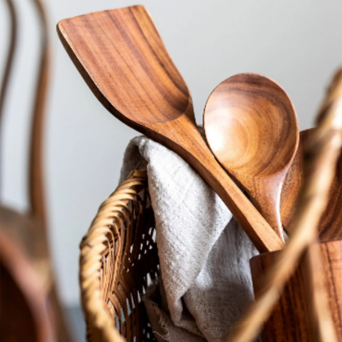 Wooden kitchen utensils set with spatula, spoon, and fork displayed with linen cloth and woven storage holder.