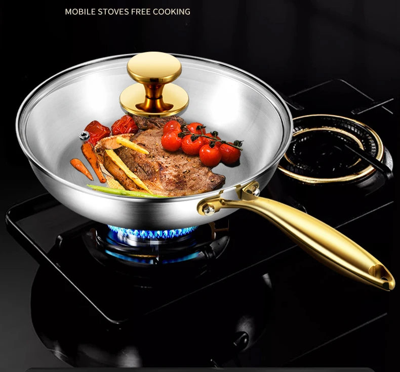 Stainless steel wok pan with golden handles cooking meat and vegetables over gas flame, featuring glass lid and non-stick sur