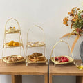 Three-tier bamboo basket stands filled with bread, lemons, and tomatoes on wooden table with dried flowers.