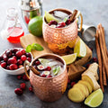 Copper Moscow mule mugs with hammered finish, filled with cranberry cocktails, garnished with fresh cranberries, lime wedges,