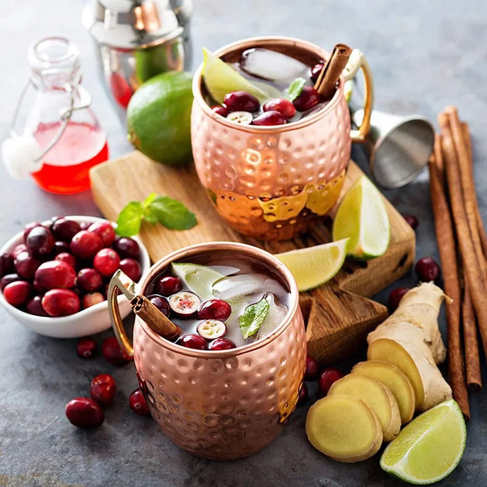 Copper Moscow mule mugs with hammered finish, filled with cranberry cocktails, garnished with fresh cranberries, lime wedges,