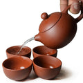 Handmade purple clay teapot pouring tea into matching cups, 200ml capacity, traditional ceramic tea set.