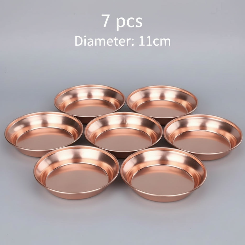 Handcrafted pure copper dining plates in nested sizes, displayed on neutral fabric with natural wood table and plant backgrou