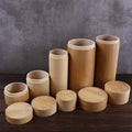 Handmade bamboo tea storage canisters with wooden lids in various sizes, arranged on dark wood surface against gray backdrop.