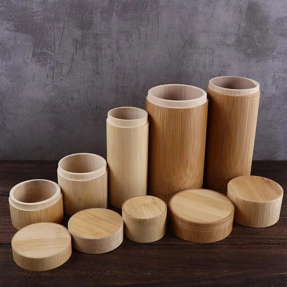 Handmade bamboo tea storage canisters with wooden lids in various sizes, arranged on dark wood surface against gray backdrop.