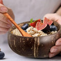 Handcrafted coconut shell bowl filled with yogurt and fresh fruits, held with wooden spoon, showcasing natural eco-friendly d