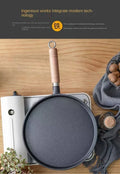 Cast iron egg skillet with wooden handle on wooden surface, surrounded by kitchen linens and cooking accessories.