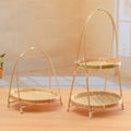 Two natural bamboo baskets with woven wicker bases and arched handles, displayed on wooden surface with warm lighting.