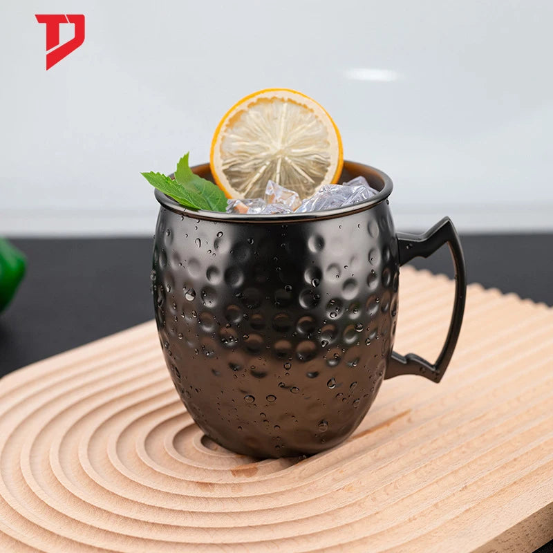 Black hammered copper insulated mug with ice, lemon slice, and mint garnish on wooden coaster