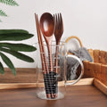 Wooden cutlery set with dark brown spoon, fork, and chopsticks displayed in clear measuring glass with wooden handles and eco