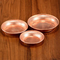 Three hammered copper serving plates in graduated sizes arranged on wooden surface, showcasing artisanal craftsmanship and re