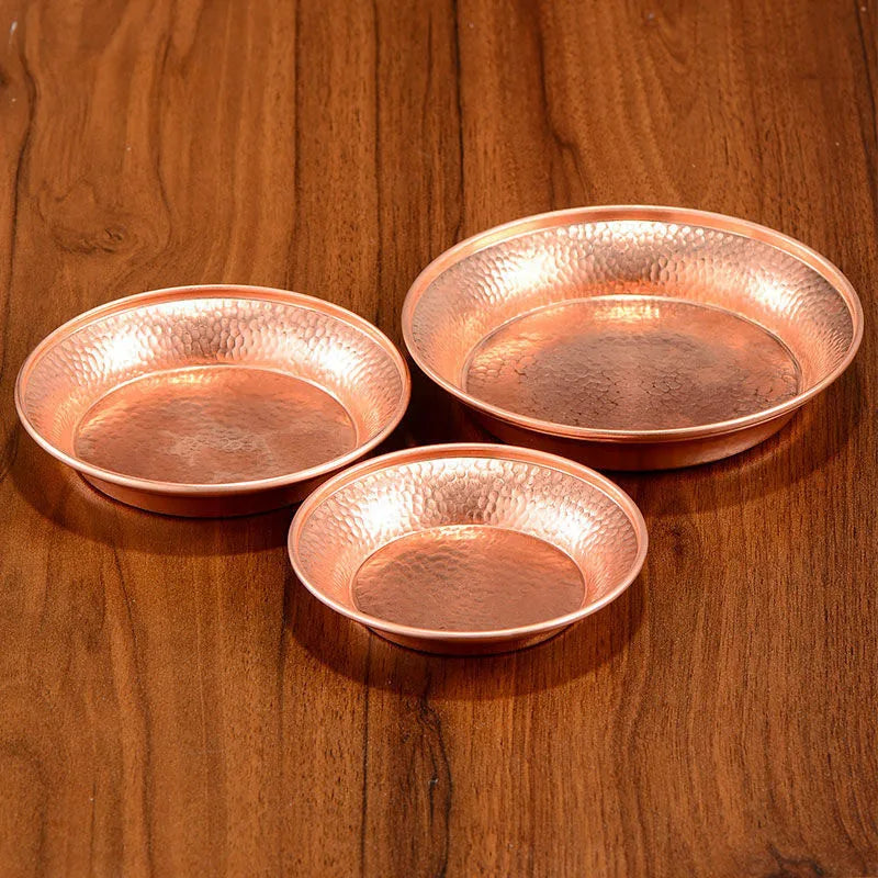 Three hammered copper serving plates in graduated sizes arranged on wooden surface, showcasing artisanal craftsmanship and re