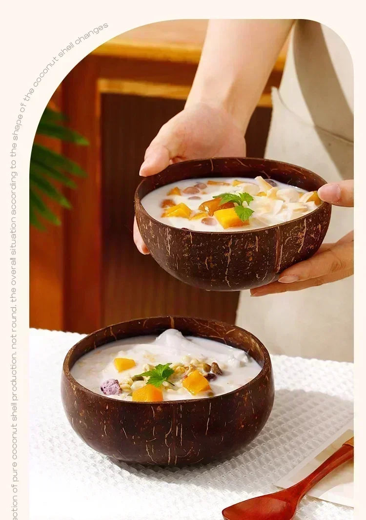Coconut wood bowls filled with creamy dessert topped with mango and herbs, held by hands in warm kitchen setting.