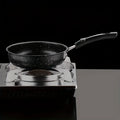 Black speckled non-stick skillet with handle on portable induction cooktop against dark background