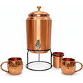 Copper water dispenser set with brass tap, metal stand, two hammered copper mugs, and glass cup on white background.