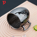 Hammered copper insulated travel cup with lid on wooden surface with lime slice and ice