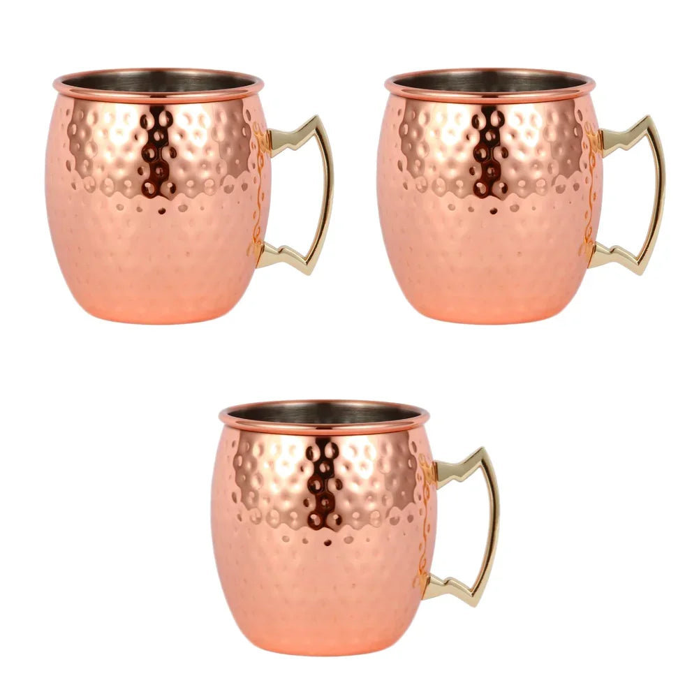 Three copper Moscow mule mugs with hammered finish, stainless steel interiors, and brass handles arranged on white background