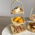Three-tier bamboo basket stand holding walnuts, mangoes, and a cream dessert with berries on white surface.