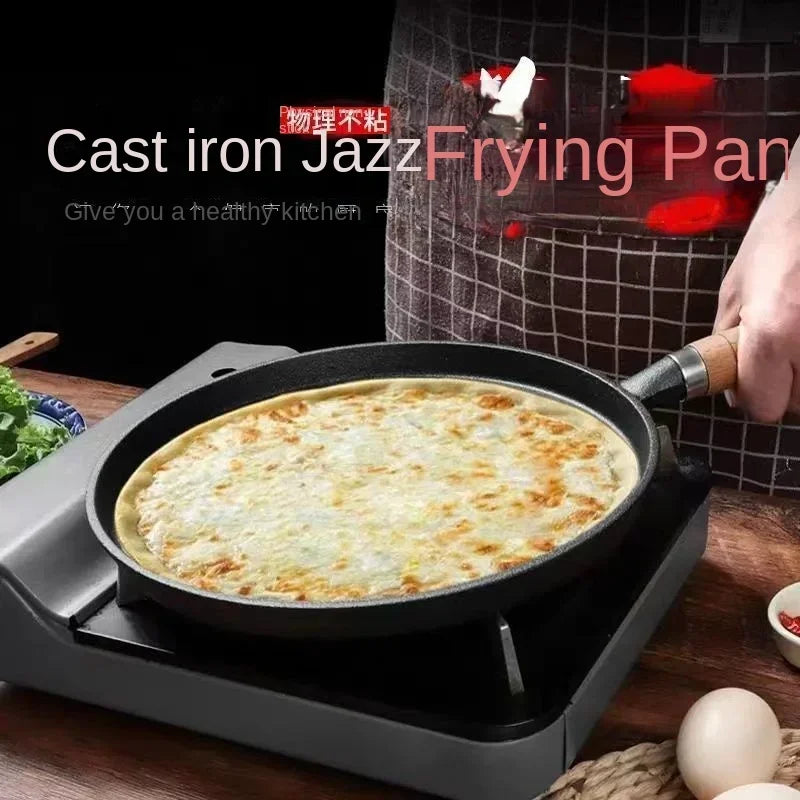 Cast iron jazz frying pan with golden-brown egg cooking on stovetop, wooden handle, black cookware on gray burner.