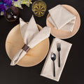 Natural cotton linen table napkins in cream displayed on beige plates with black cutlery and decorative flowers on dark backg